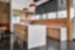 Modern office kitchen or break room with a large island, bar seating, and open shelving. Office design by Henricksen.